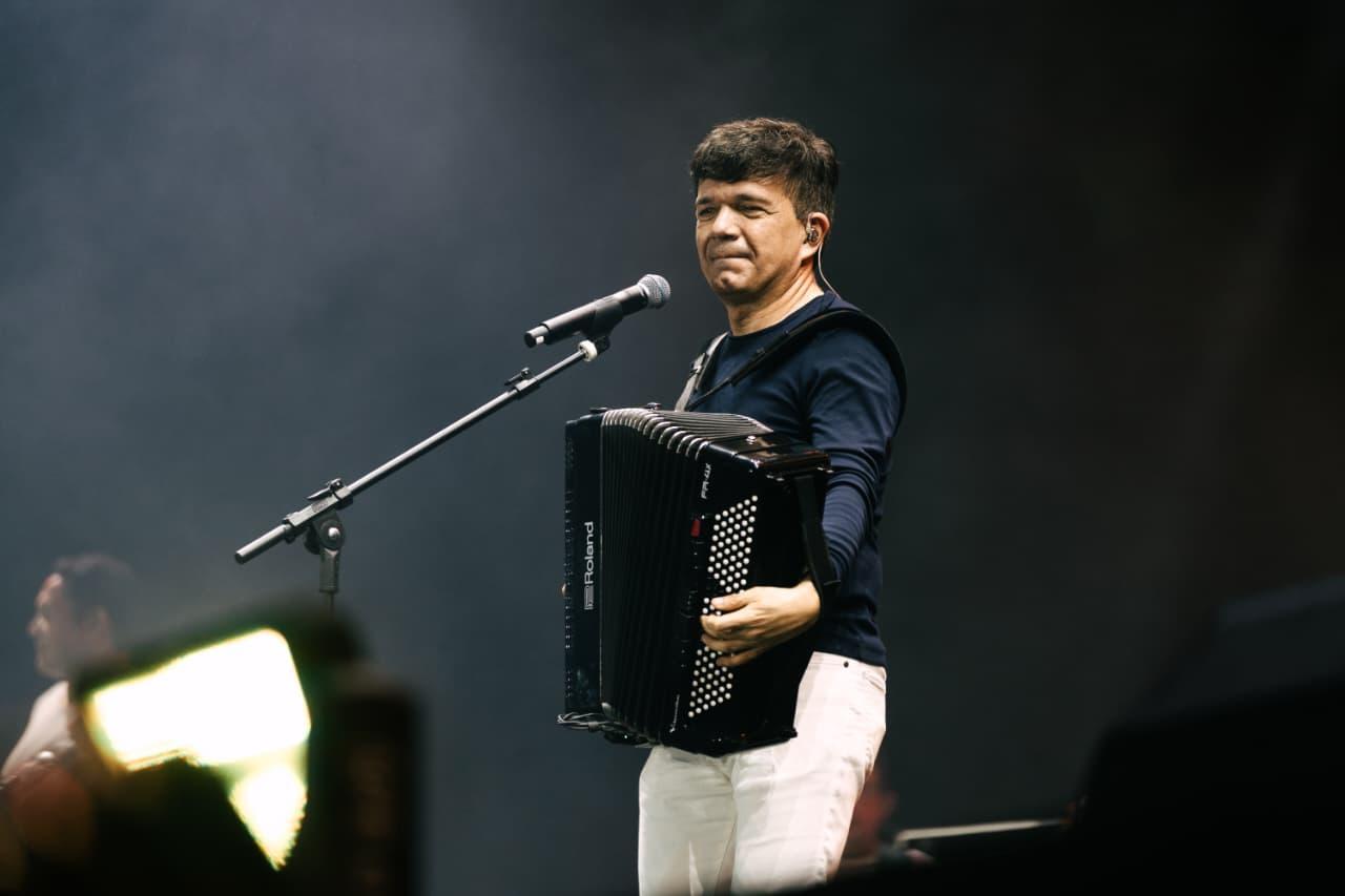 Músico masculino tocando acordeão em palco escuro com microfone à frente. O músico é Waldonys.