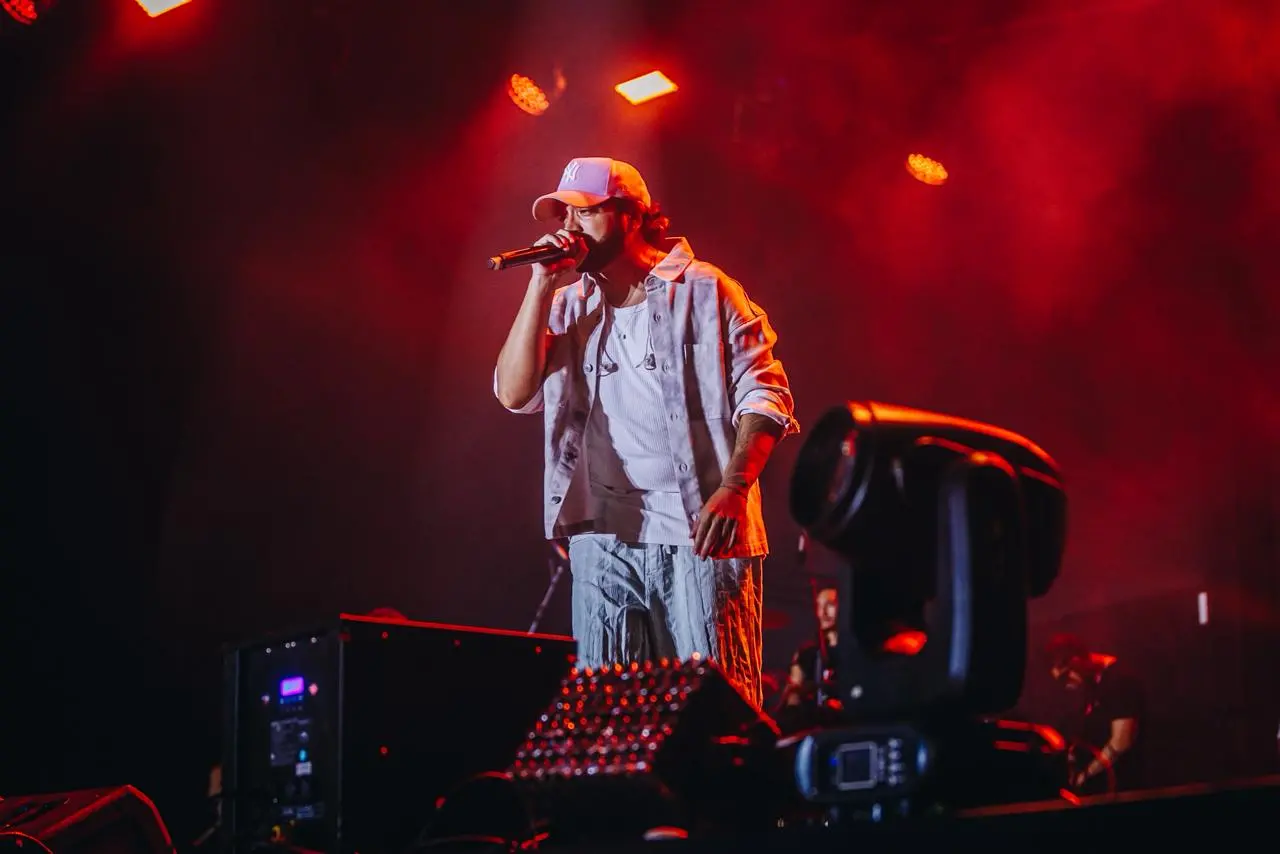 Homem performando ao vivo em show de música, com foco no vocalista e luzes de palco avermelhadas.