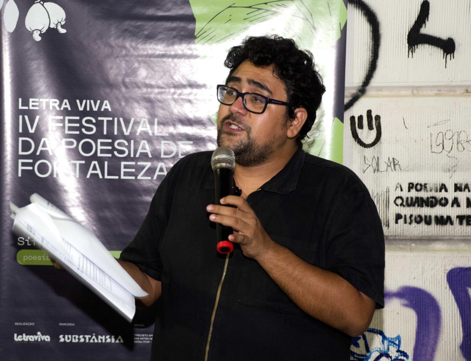Talles Azigon com um livro e microfone na mão no Festival de Poesia de Fortaleza.