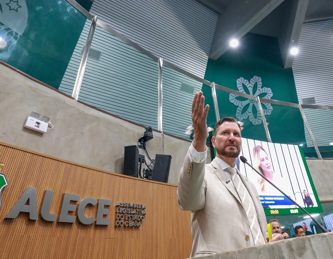Romeu Aldigueri durante discurso na Assembleia Legislativa do Ceará no final do ano passado, enquanto imagem de Tainah Marinho aparece no telão.