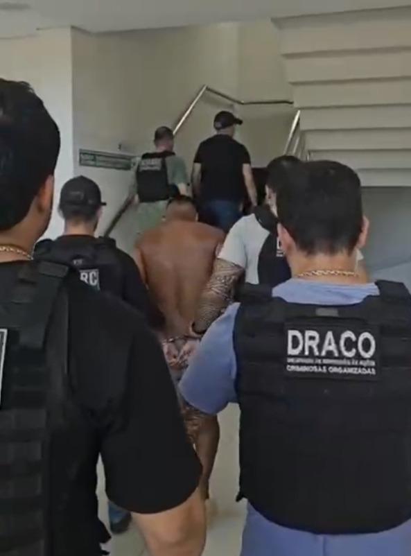 A imagem mostra um homem sem blusa, sendo preso, cercado por seis policiais civis, dentro de uma delegacia do Ceará.
