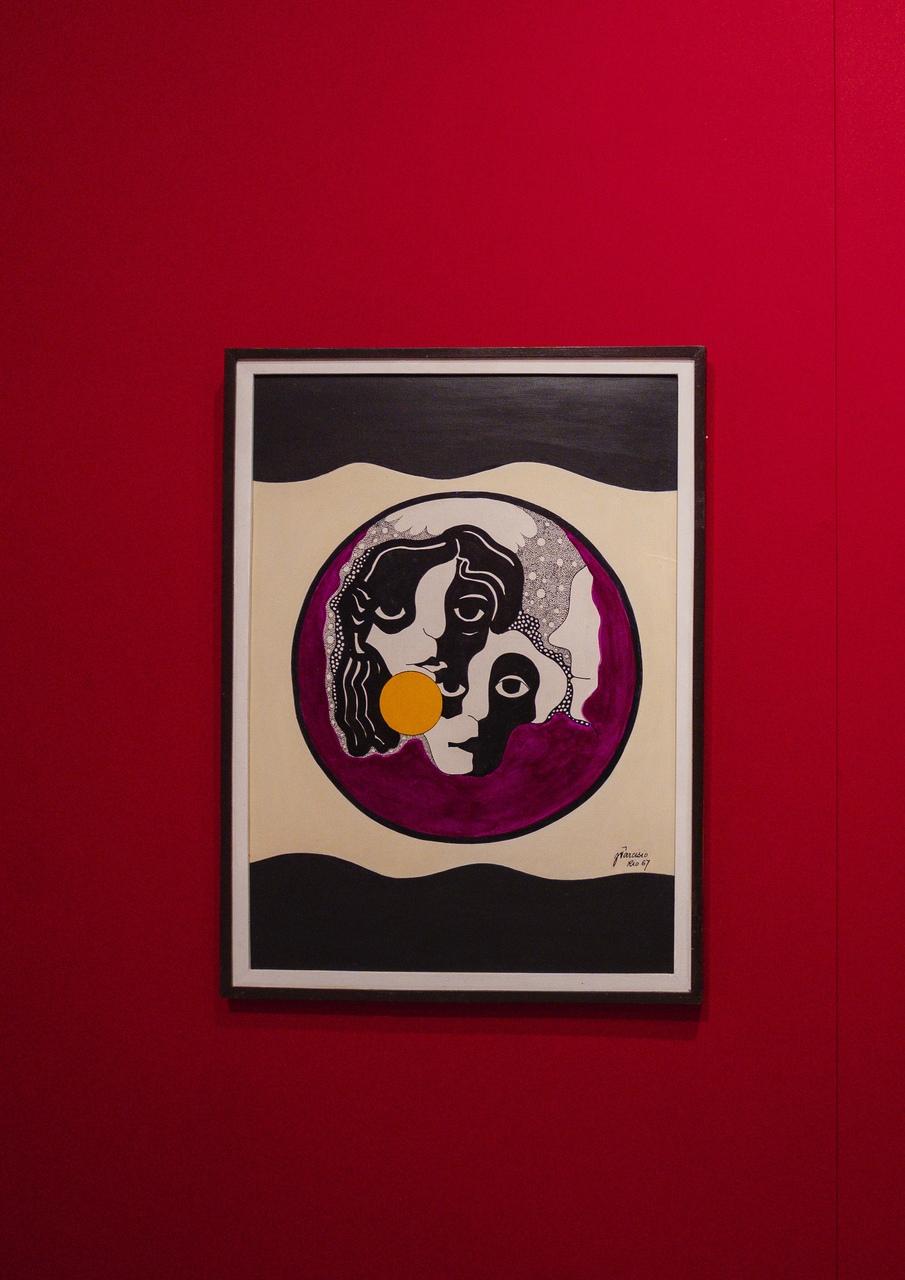 Obra de arte de Zé Tarcísio colocada em parede vermelha de espaço de exposição de arte.