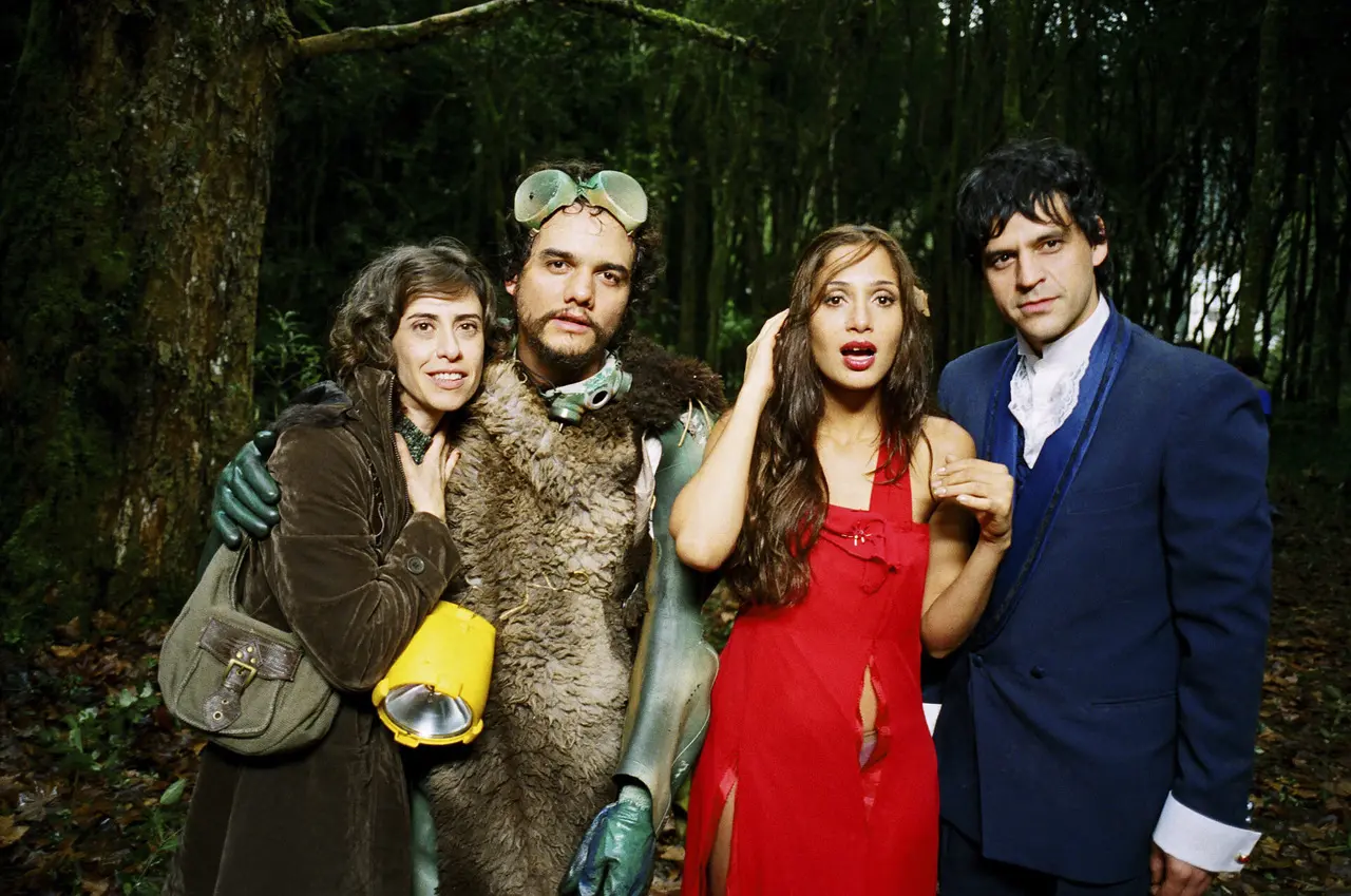 Os atores Fernanda Torres, Wagner Moura, Camila Pitanga e Bruno Garcia posam em uma floresta densa vestindo figurinos peculiares para o filme 'Saneamento Básico, O Filme'. A composição destaca o contraste entre os trajes improvisados de ficção científica e de época sob a luz natural, criando uma cena vibrante e lúdica em meio à vegetação.