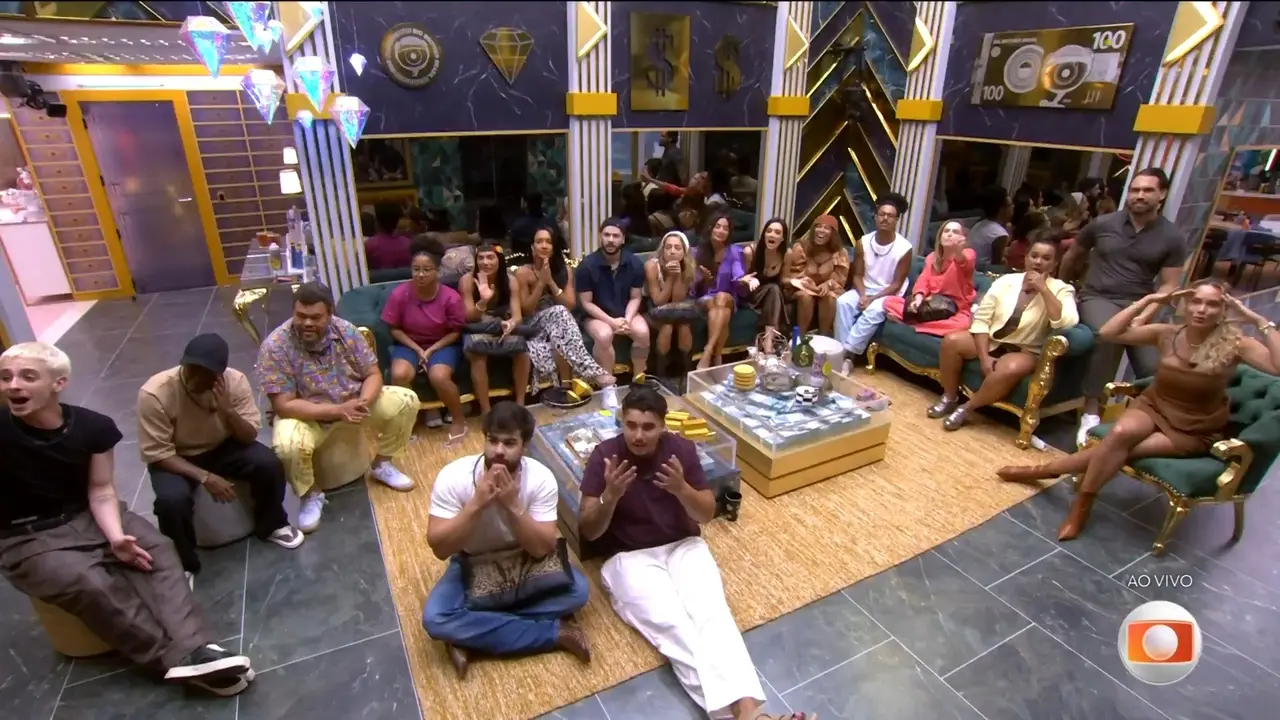 O elenco do BBB 26 aparece reunido nos sofás de veludo verde da sala, que possui uma decoração luxuosa inspirada em cofres e moedas de ouro. A composição destaca a expressão dos participantes durante uma transmissão ao vivo, sob luzes em formato de diamantes e paredes com texturas de mármore escuro.