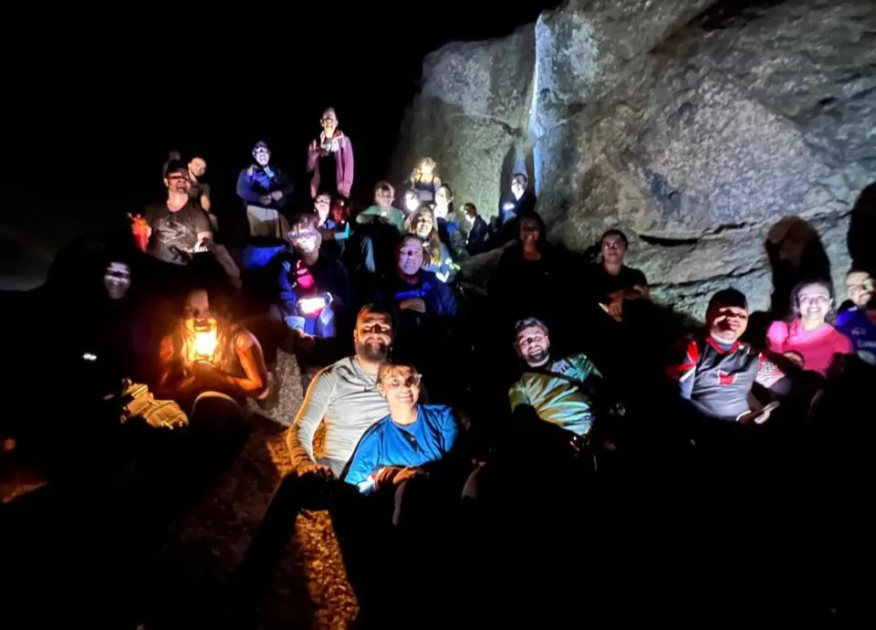 Grupo de pessoas explorando uma a Trilha da Pedra do ET, em Quixadá, com lanternas, usando roupas adequadas e sorrindo, em uma aventura de passeio em cavernas subterrâneas.