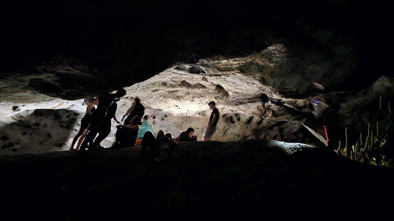 Grupos de pessoas explorando uma caverna em Quixadá, no Ceará, com iluminação em destaque na parede rochosa, criando uma atmosfera de aventura e exploração subterrânea.
