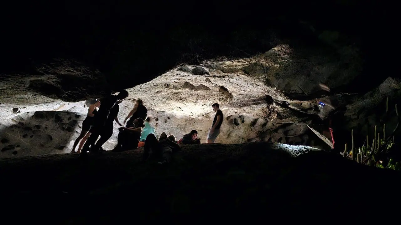 Grupos de pessoas explorando uma caverna em Quixadá, no Ceará, com iluminação em destaque na parede rochosa, criando uma atmosfera de aventura e exploração subterrânea.