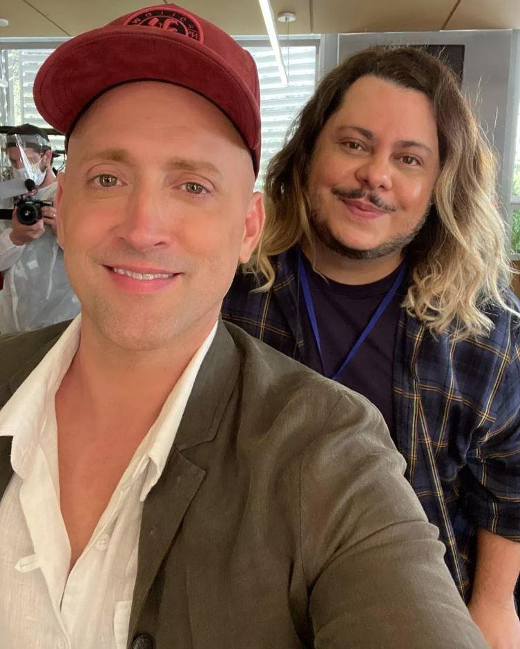 Paulo Gustavo com boné vermelho e terno, enquanto Majella aparece com blusa quadriculada e cabelo loiro longo.