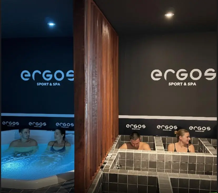 Na imagem, montagem comparativa do Ergos Sport & Spa. À esquerda, um casal relaxa em uma hidromassagem com iluminação azul. À direita, os dois aparecem em tanques individuais de imersão feitos de azulejos escuros. O ambiente é moderno, com paredes cinzas e logotipos da marca em evidência.