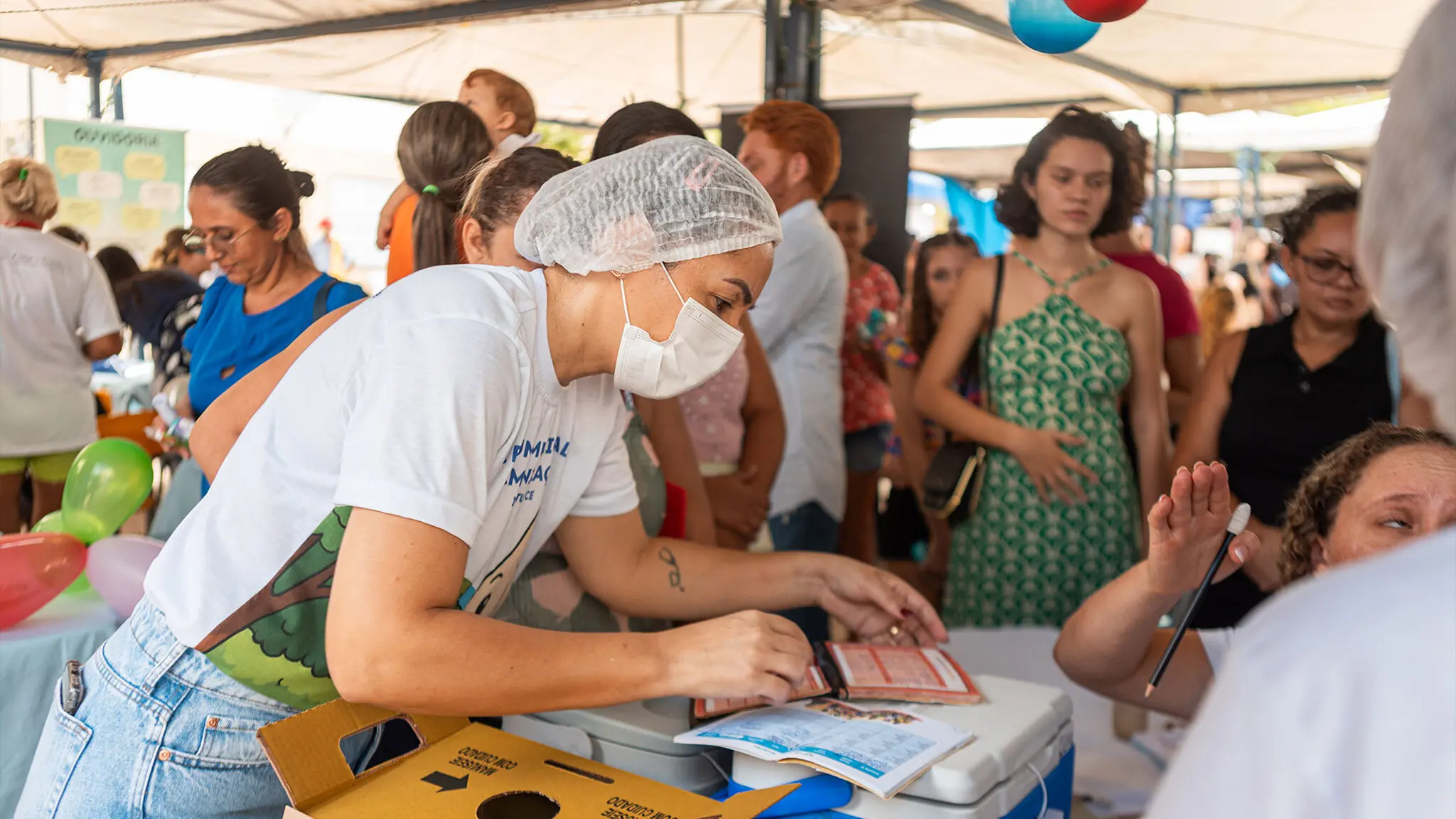 Mulher, usando touca e máscara, presta atendimento ao público em evento da Prefeitura de Iguatu.