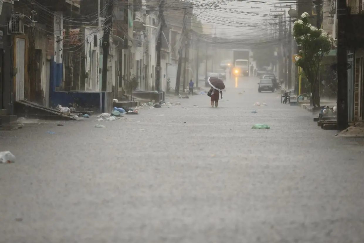 Rua alagada com figura de pedestre bem ao fundo com guarda chuva e água até o joelho.