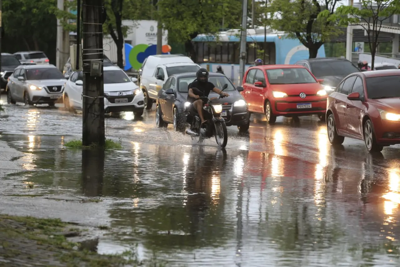 Avenida com muita água de chuva e vários carros.