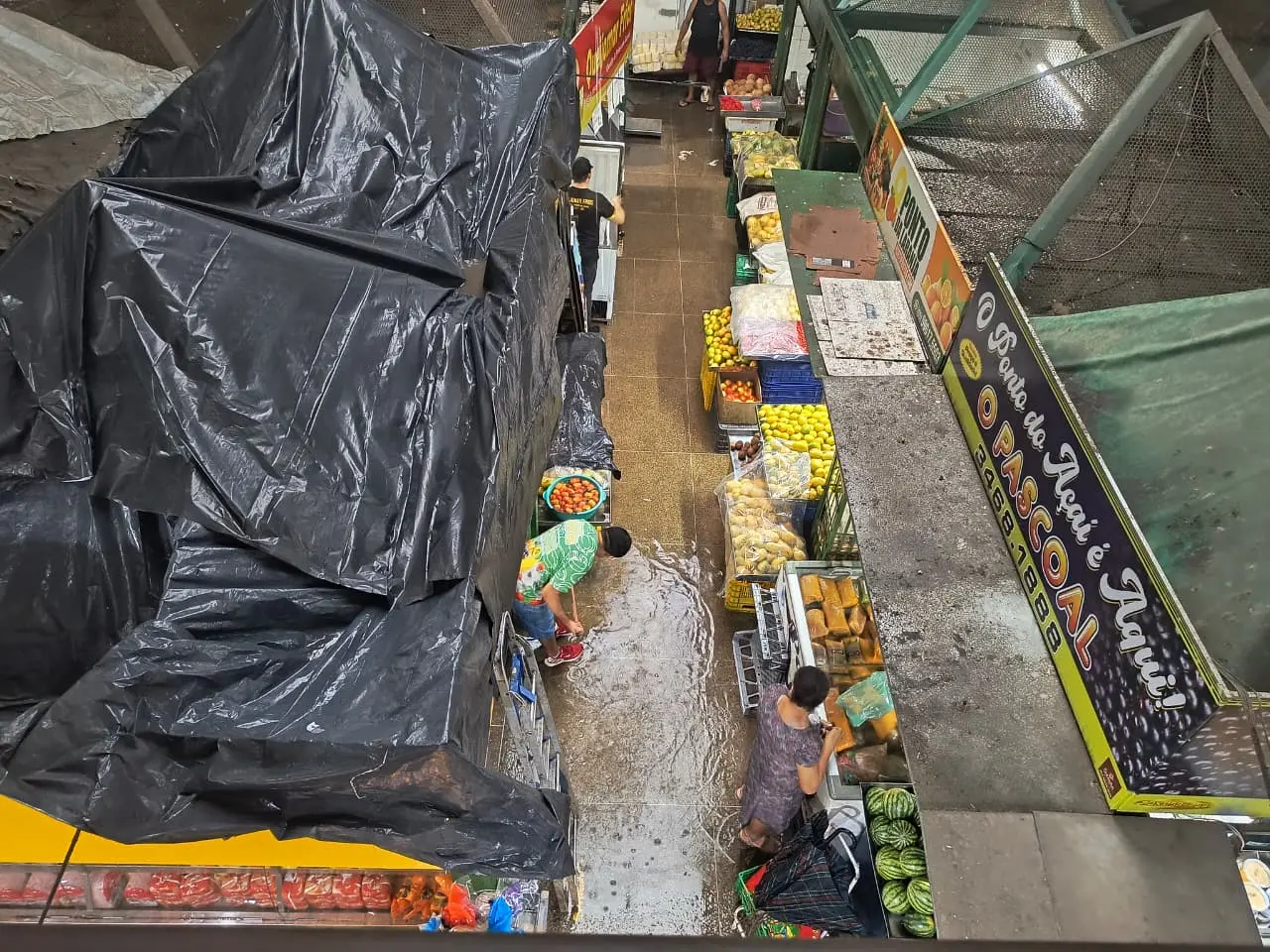 Foto aérea de mercado com quiosques fechados e água alagando o chão.