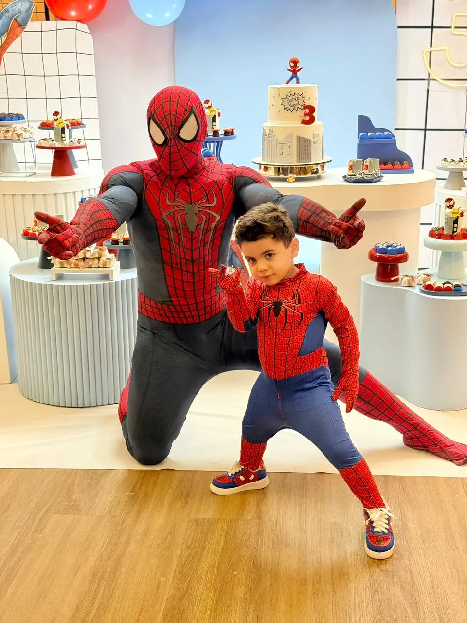 Na imagem, um menino de aproximadamente 3 anos está de pé, fazendo o gesto clássico de 