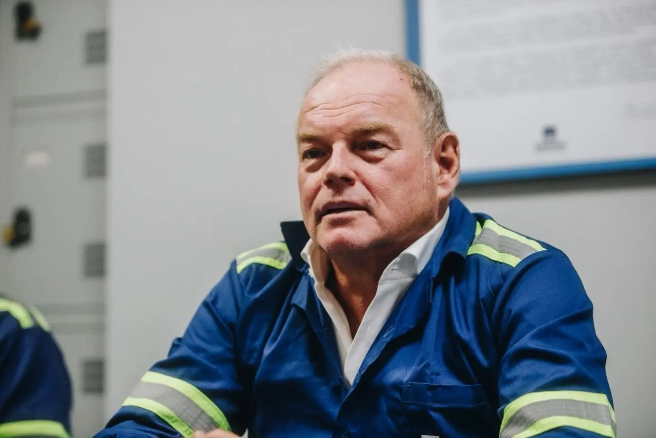 Presidente do Conselho de Administração da Gerdau, André Gerdau Johannpeter. Homem usando uniforme industrial azul, sentado em ambiente interno de fábrica.