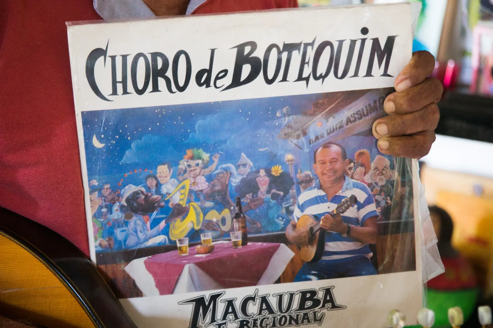 Na imagem, uma pessoa segura a capa de um disco de vinil intitulado 