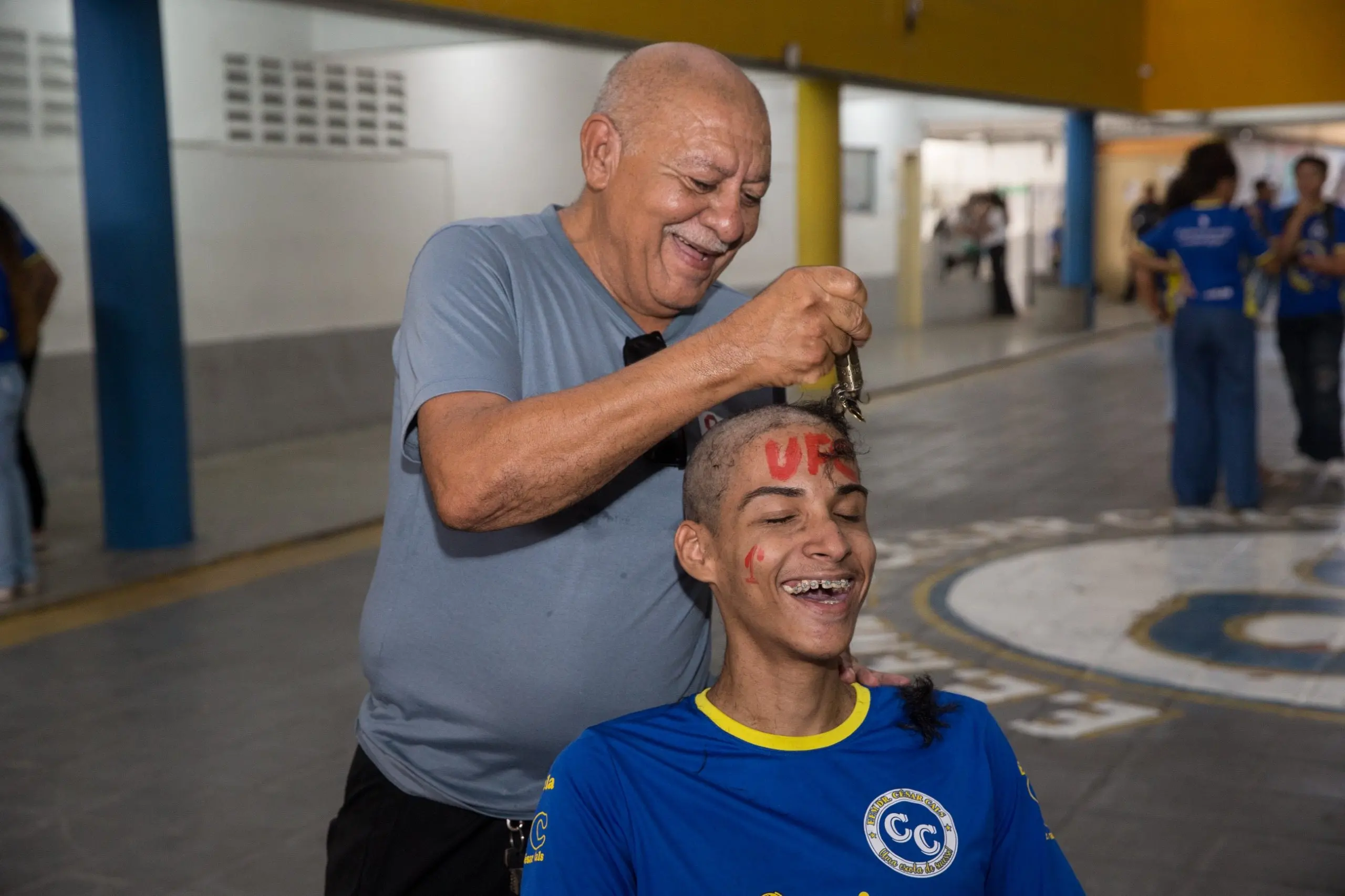 Em clima de festa, um jovem celebra sua aprovação na Universidade Federal do Ceará participando do tradicional rito de raspar a cabeça. O momento, registrado em uma escola pública, simboliza o encerramento de um ciclo de estudos e o início da trajetória acadêmica.