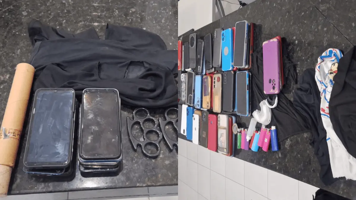 Objetos apreendidos expostos sobre bancada, incluindo vários celulares, capas de telefone, carregadores, isqueiros, luvas, socos ingleses e pedaços de tecido escuro.