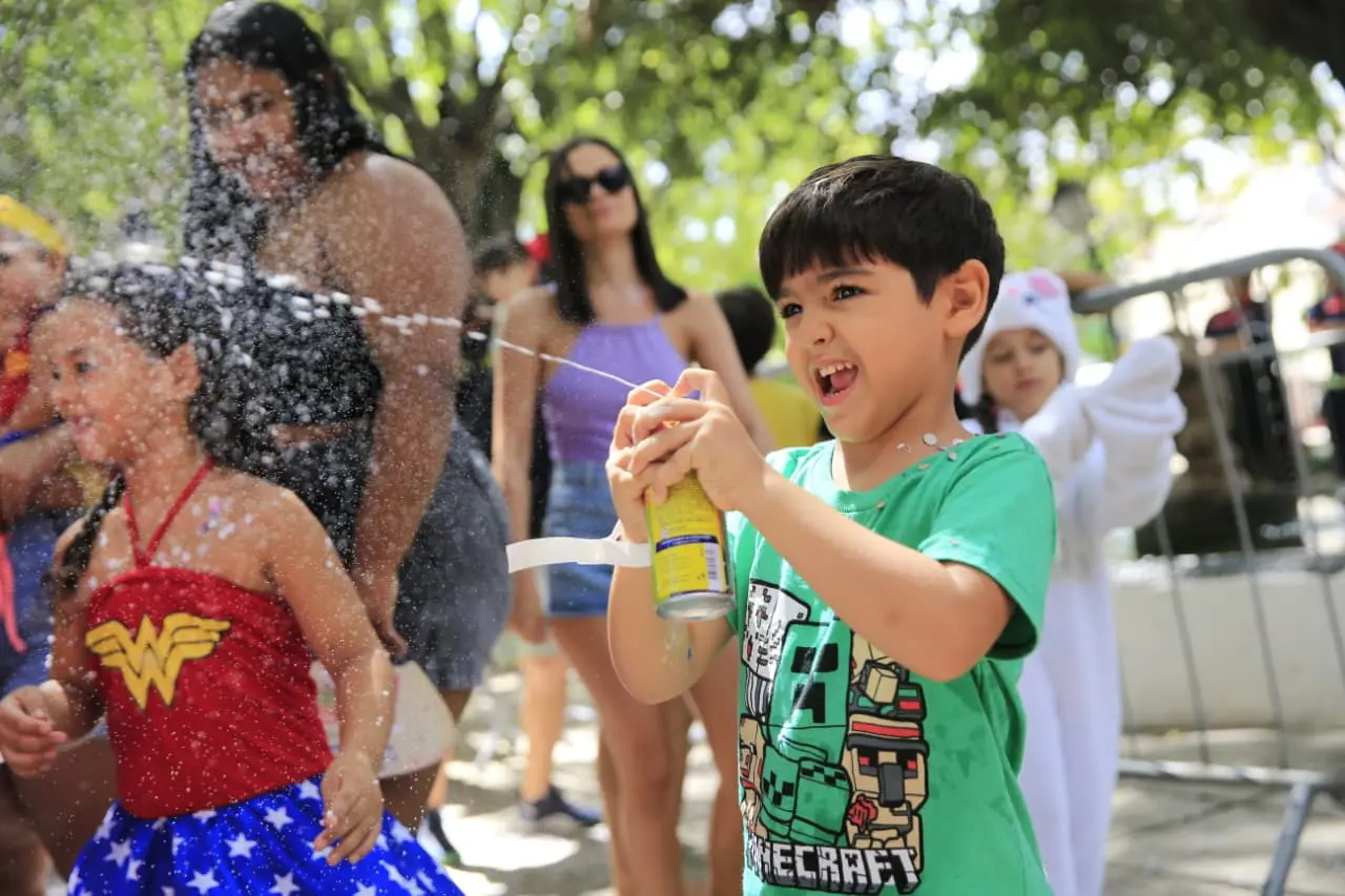 Menino com blusa verde usando espuminha em festa de Carnaval.