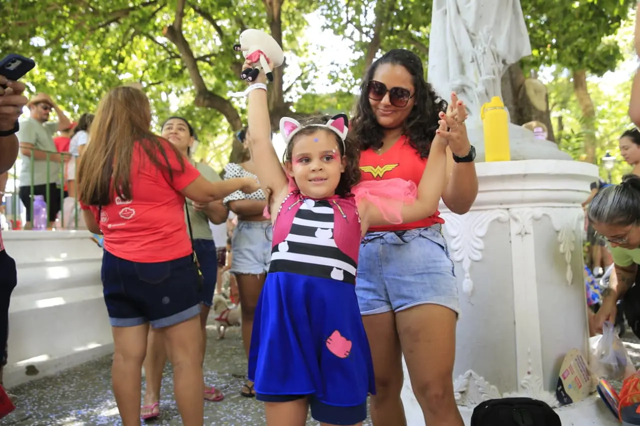 Criança fantasiada de Gabby, com short azul, blusa listrada e colete rosa.