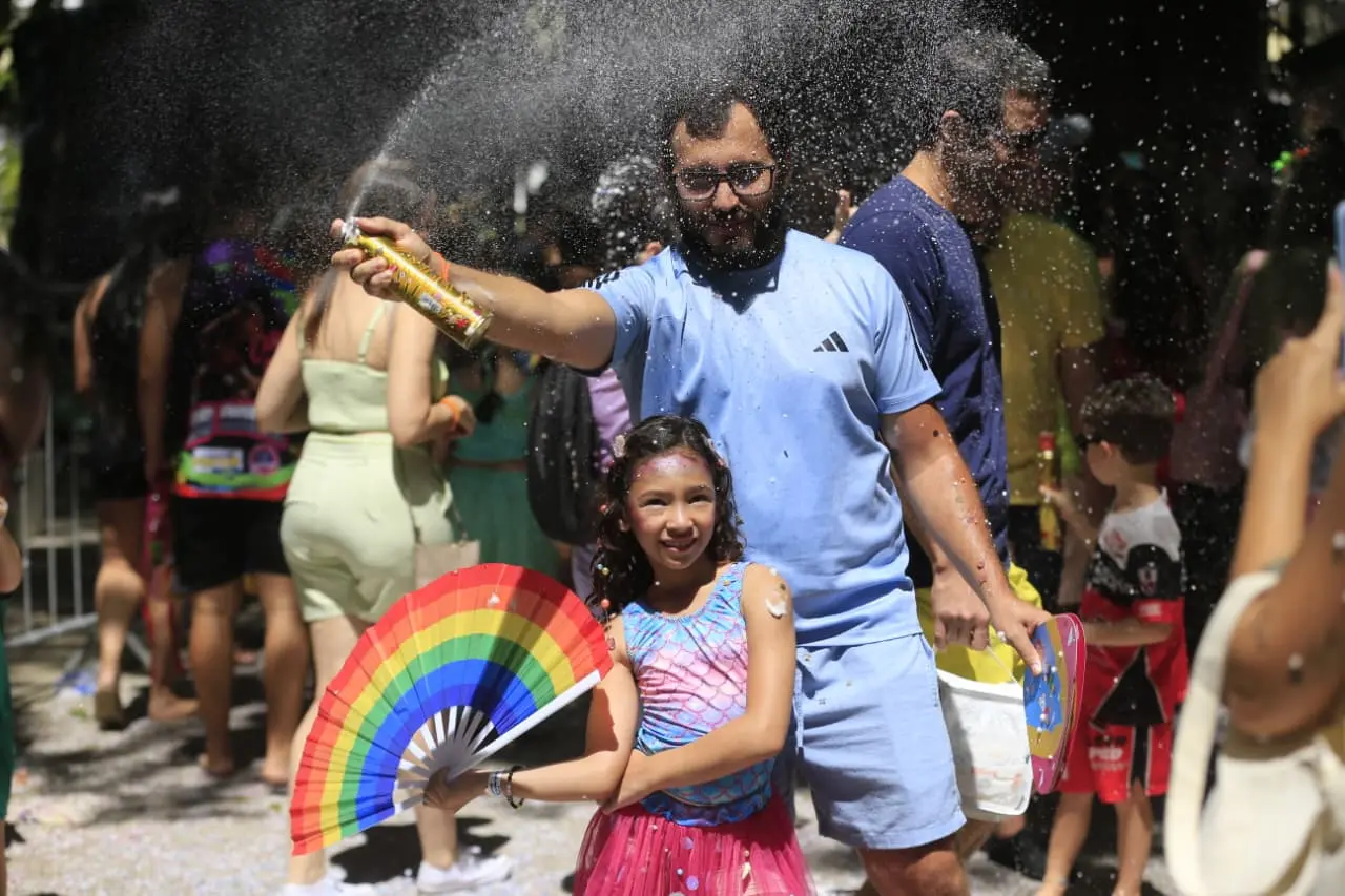 Menina com leque da cor do arco-íris na frente de adulto usando espuminha.