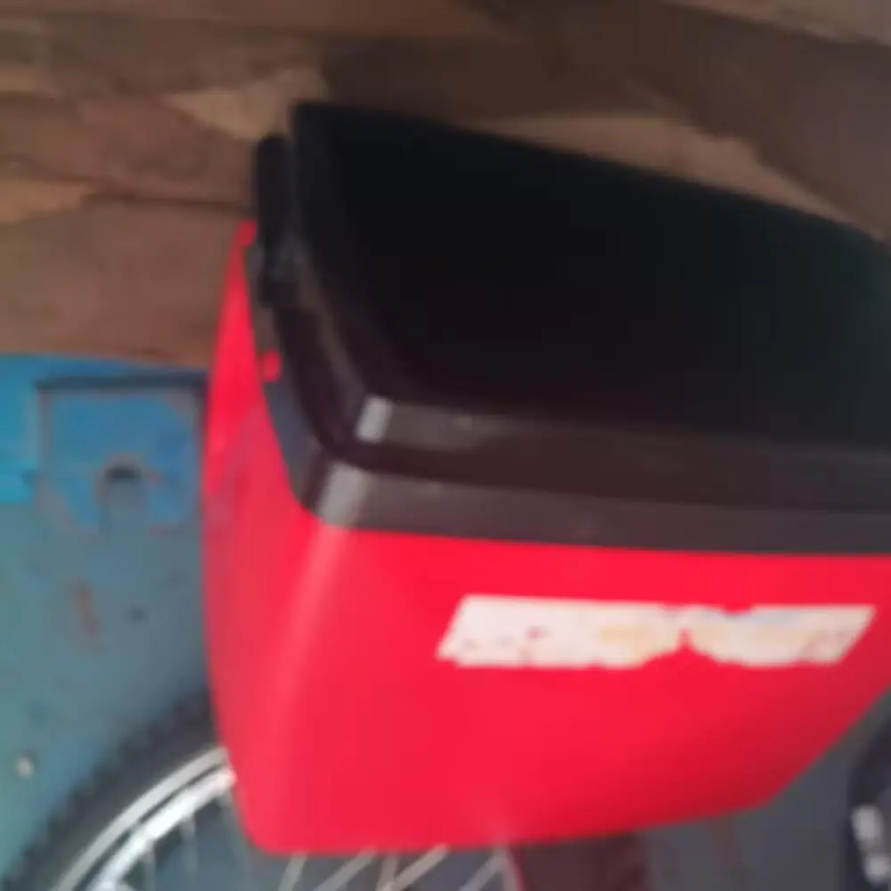 Cooler vermelho com tampa preta preso à parte traseira de uma bicicleta, visto de perto.