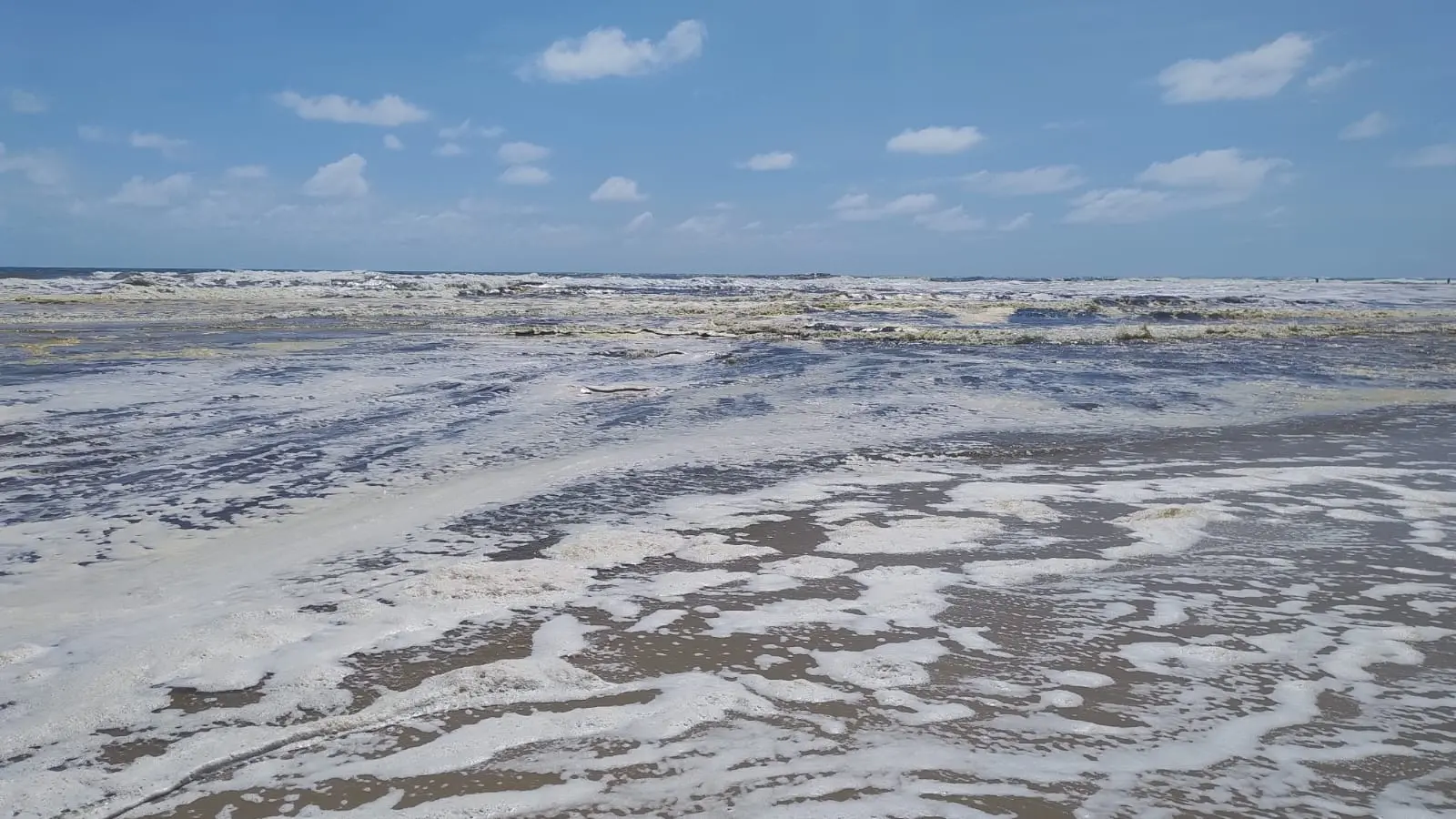 Foto aberta do mar da Praia do Futuro, em Fortaleza, com a água cheia de espuma marrom e branca.