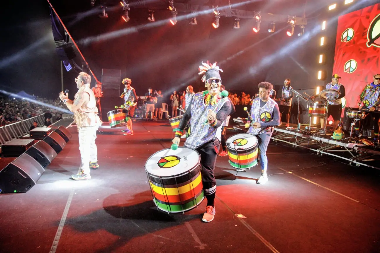 Show do Olodum Fortaleza. Palco iluminado com cores vermelhas e público na areia.
