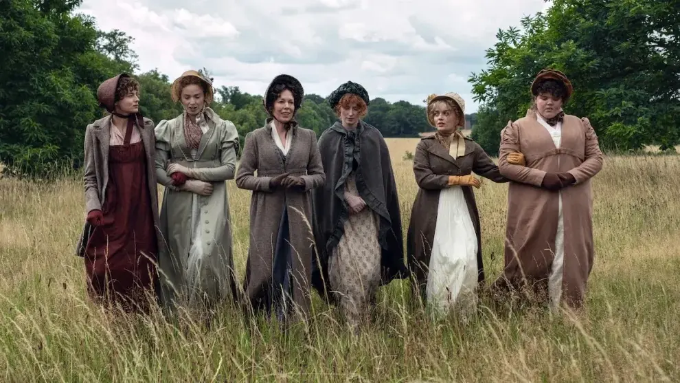 Imagem de divulgação da série Orgulho e Preconceito, da Netflix, estrelada por Jack Lowden, onde destaca seis mulheres caminhando lado a lado por um campo de gramas altas, vestindo trajes de época. O grupo avança sob um céu nublado em uma composição que destaca a elegância clássica da produção e a interação serena entre as personagens em meio à natureza.