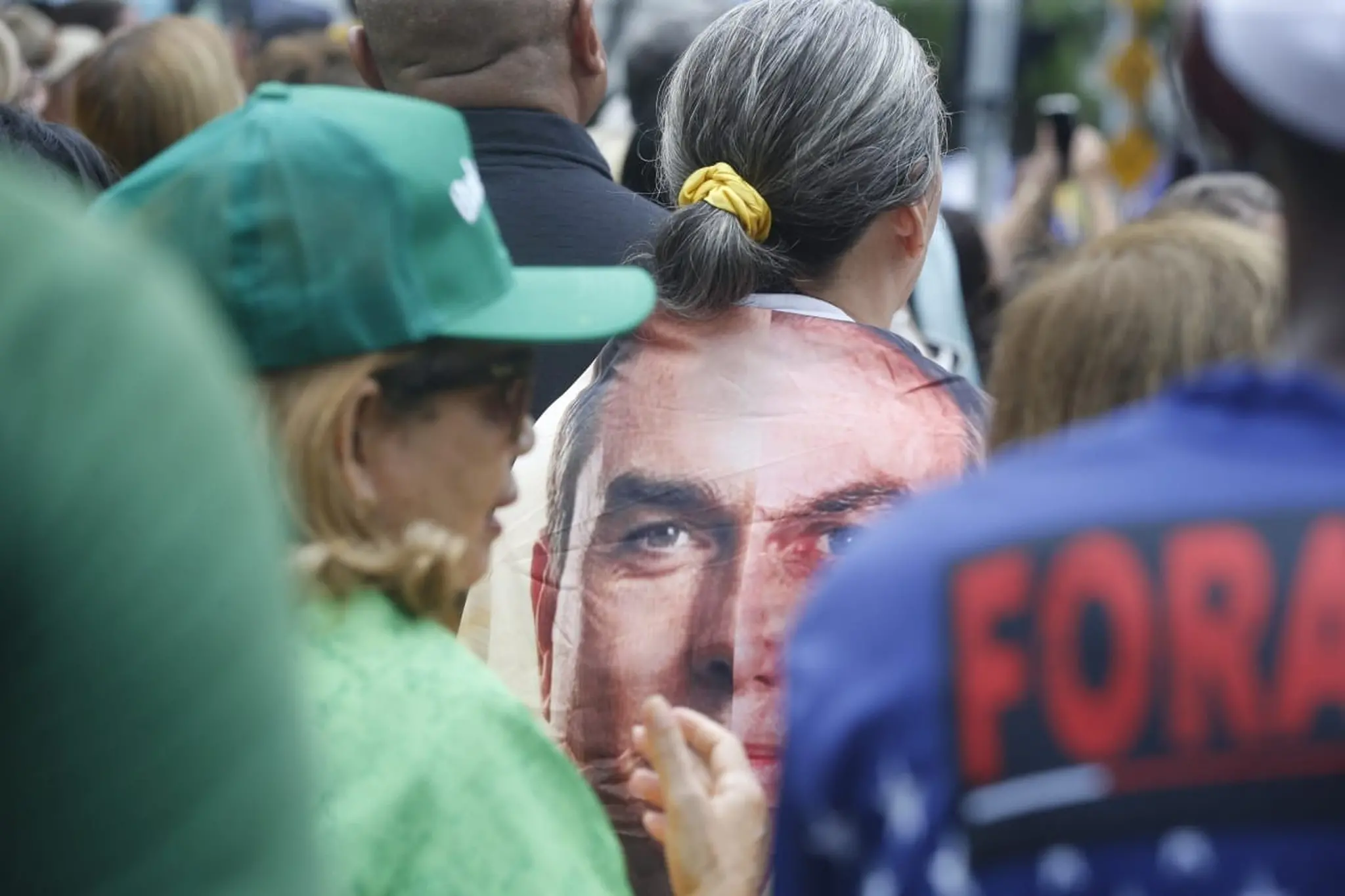 Pessoa de costas, enrolada com um tecido com o rosto de Flávio Bolsonaro, senador e pré-candidato à presidência.