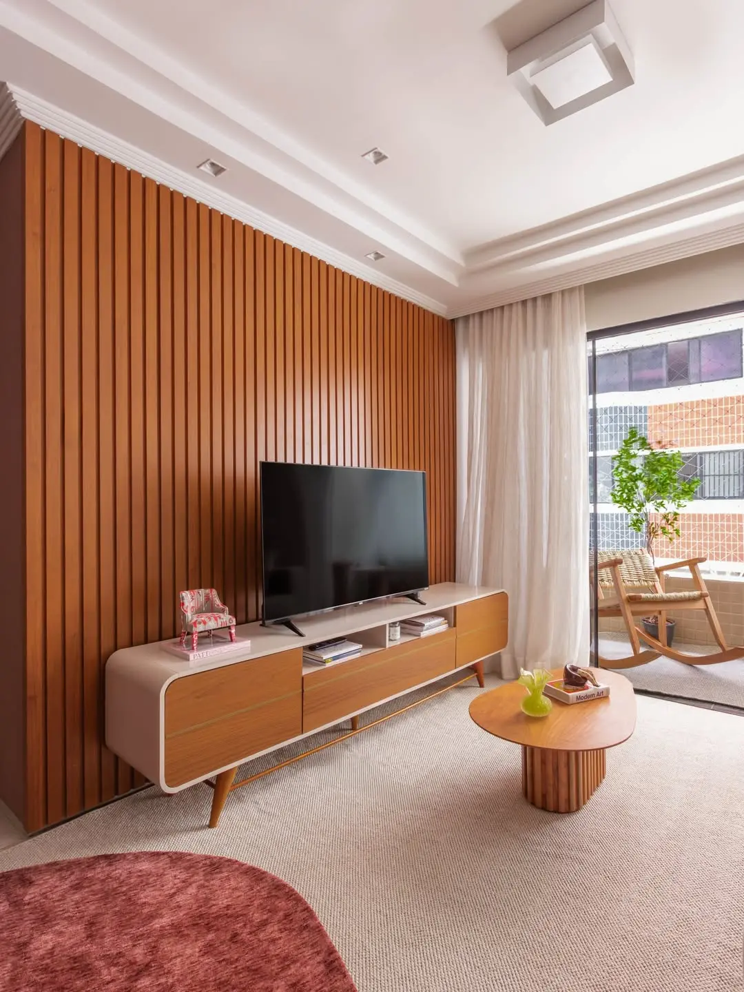 Sala com painel ripado, móveis soltos e cadeira de balanço na varanda.