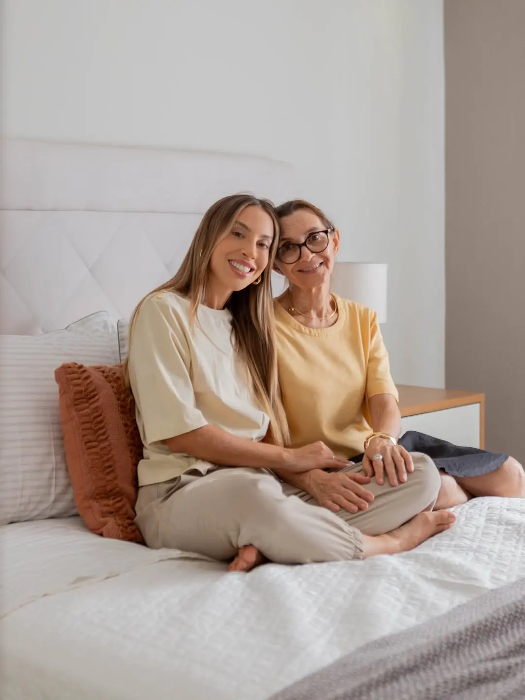 Renata e a mãe posam sentada em cama.
