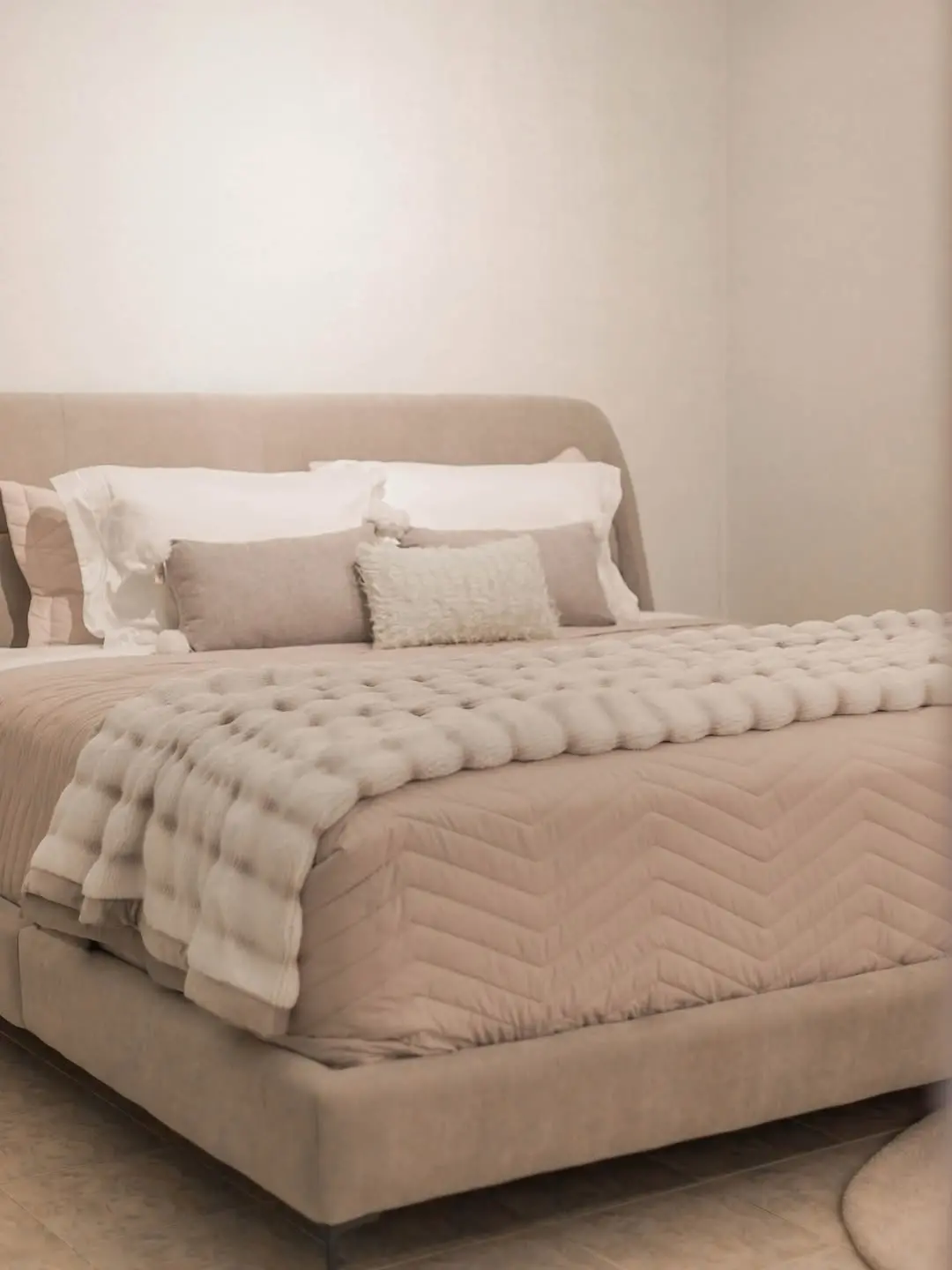 Cama com edredom e manta em tons de cinza e travesseiros brancos.