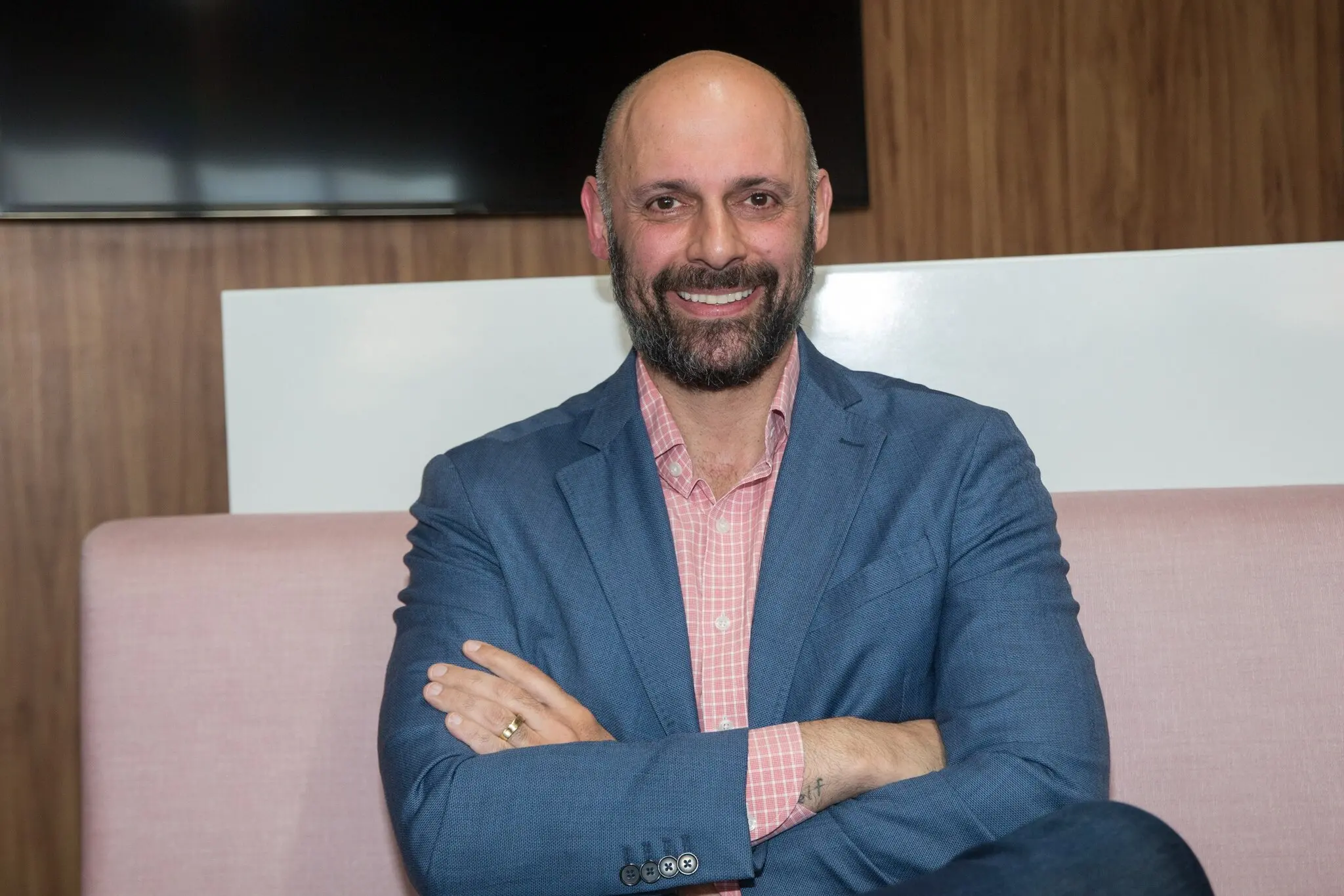 Homem de camisa rosa e blazer azul, olhando para a câmera e sorrindo.