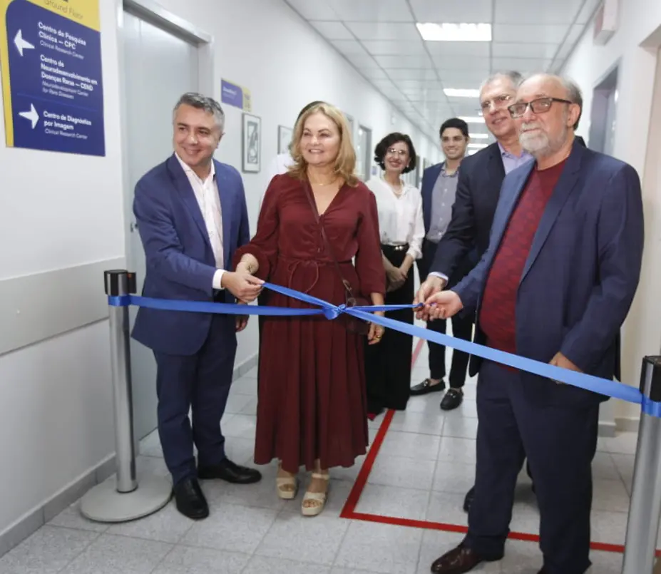 Autoridades inauguram o Centro de Neurodesenvolvimento em Doenças Raras (Cend) cortando uma fita azul em um corredor de hospital. Ao fundo, placas de sinalização identificam as alas da unidade.
