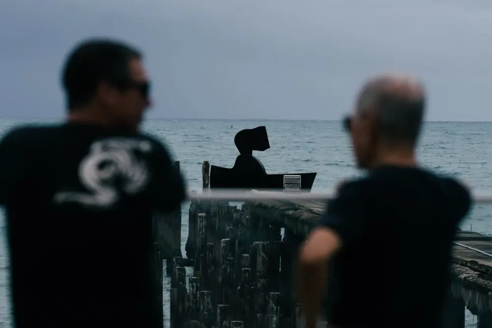 Na imagem, fotografia em plano médio com profundidade de campo reduzida. No fundo, centralizada e em foco, está a escultura preta 