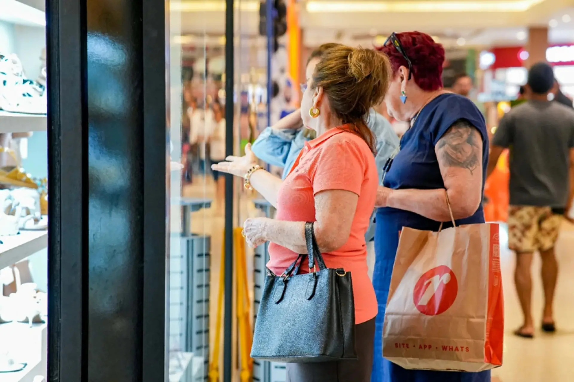 Grupo de três mulheres olham vitrine.