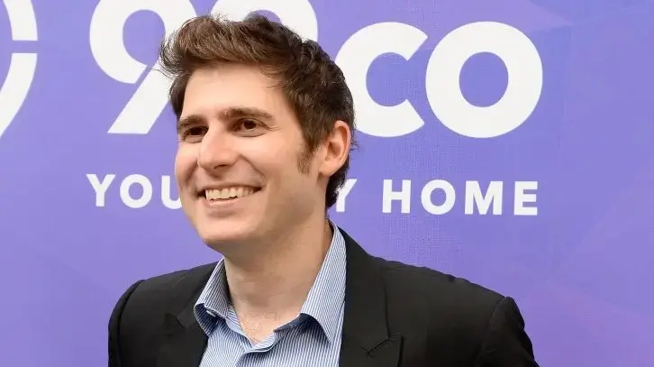 O empresário Eduardo Saverin posa para foto. Ele sorri e olha para o horzionte. Ele veste um blazer e uma camisa de botão.