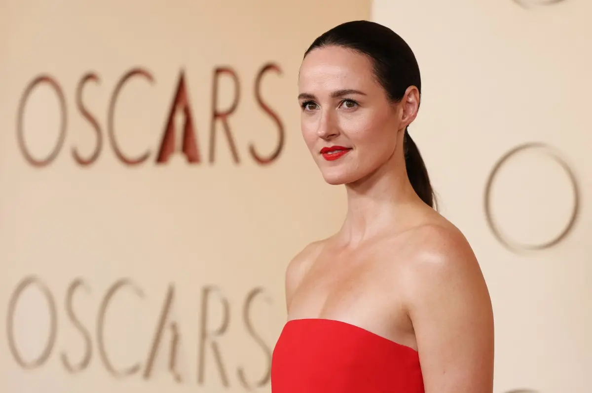 Pessoa usando vestido vermelho tomara que caia, com cabelo preso e posando diante do painel do Oscar.