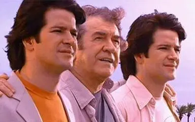 Três homens estão lado a lado ao ar livre, olhando para a mesma direção com expressões atentas; o homem mais velho está no centro, enquanto os dois mais jovens o acompanham.