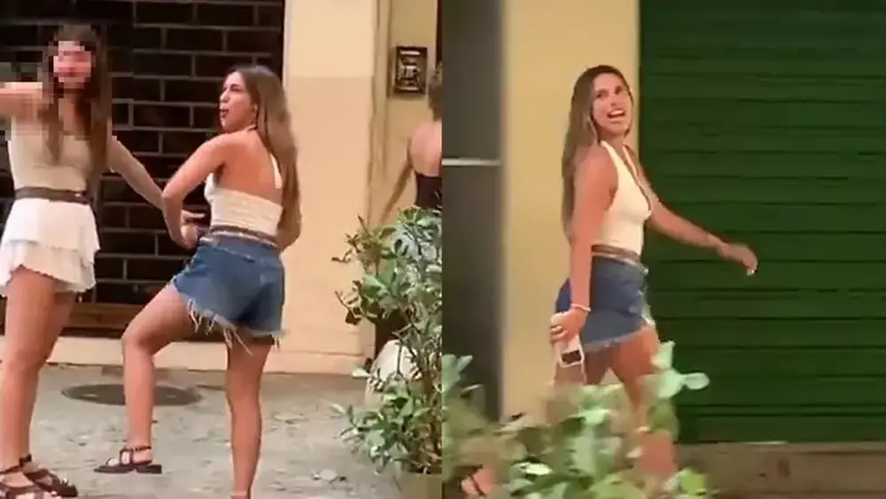 Na imagem, montagem com duas fotos lado a lado mostrando o flagrante de uma mulher em uma rua urbana. À esquerda, a mulher aparece de perfil, vestindo um top branco frente única e shorts jeans curtos; ela está com o corpo levemente inclinado para frente e as mãos próximas aos quadris. Atrás dela, outra mulher com o rosto desfocado estende o braço. À direita, a mesma mulher de top branco é vista caminhando e olhando para trás com uma expressão de deboche ou riso, segurando um celular na mão. O cenário ao fundo mostra portas de estabelecimentos fechadas e uma planta em um vaso.