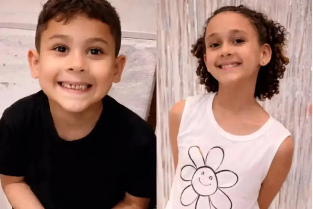 Na imagem, montagem com duas fotos individuais de crianças sorridentes, lado a lado. À esquerda: Um menino de pele clara e cabelos castanhos curtos e ondulados. Ele veste uma camiseta preta e sorri abertamente para a câmera, mostrando os dentes. O fundo é uma parede clara com textura. À direita: Uma menina de pele clara e cabelos castanhos cacheados na altura dos ombros. Ela veste uma regata branca com o desenho de uma flor sorridente no centro. Ela sorri de forma gentil, usando pequenos brincos. O fundo é composto por fitas metálicas prateadas, semelhantes a uma decoração de festa. No canto inferior direito, há uma pequena marca d'água de reprodução.