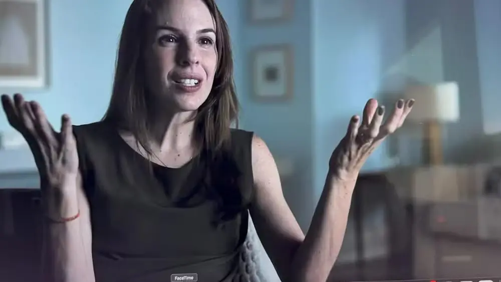 Mulher explicando algo com expressão facial e gestos em ambiente interno, possivelmente uma entrevista ou conversa casual.