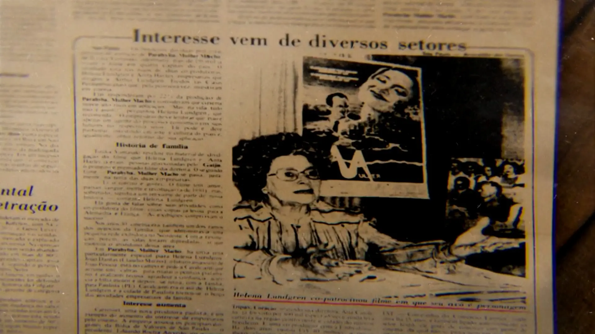 Página de jornal antiga apresentada na série 'O Testamento - O Segredo de Anita Harley' mostra a manchete 'Interesse vem de diversos setores' e destaca uma fotografia de Helena Lundgren gesticulando em frente a um cartaz de cinema.