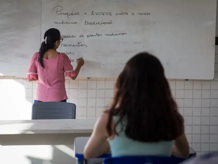 professor de costas, escrevendo em um quadro branco.