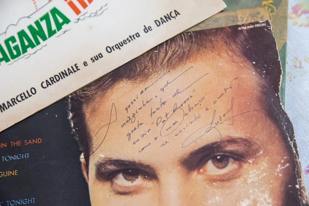 Na imagem, close-up da capa desgastada de um disco de vinil antigo, mostrando o rosto de um homem de olhos claros. Na testa da imagem do homem, há uma dedicatória escrita à mão com caneta azul que diz: 