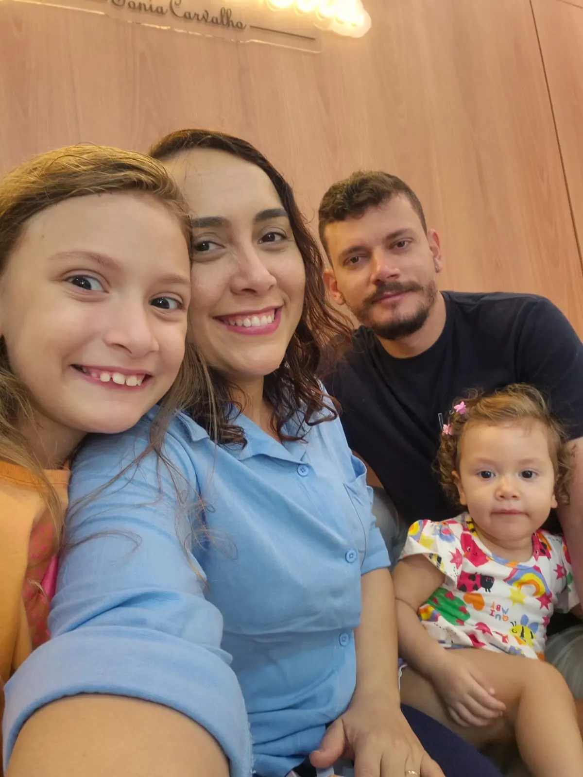 Na imagem, uma fotografia em plano médio, tirada de um ângulo ligeiramente inferior, captura uma família de quatro pessoas em uma pose de 