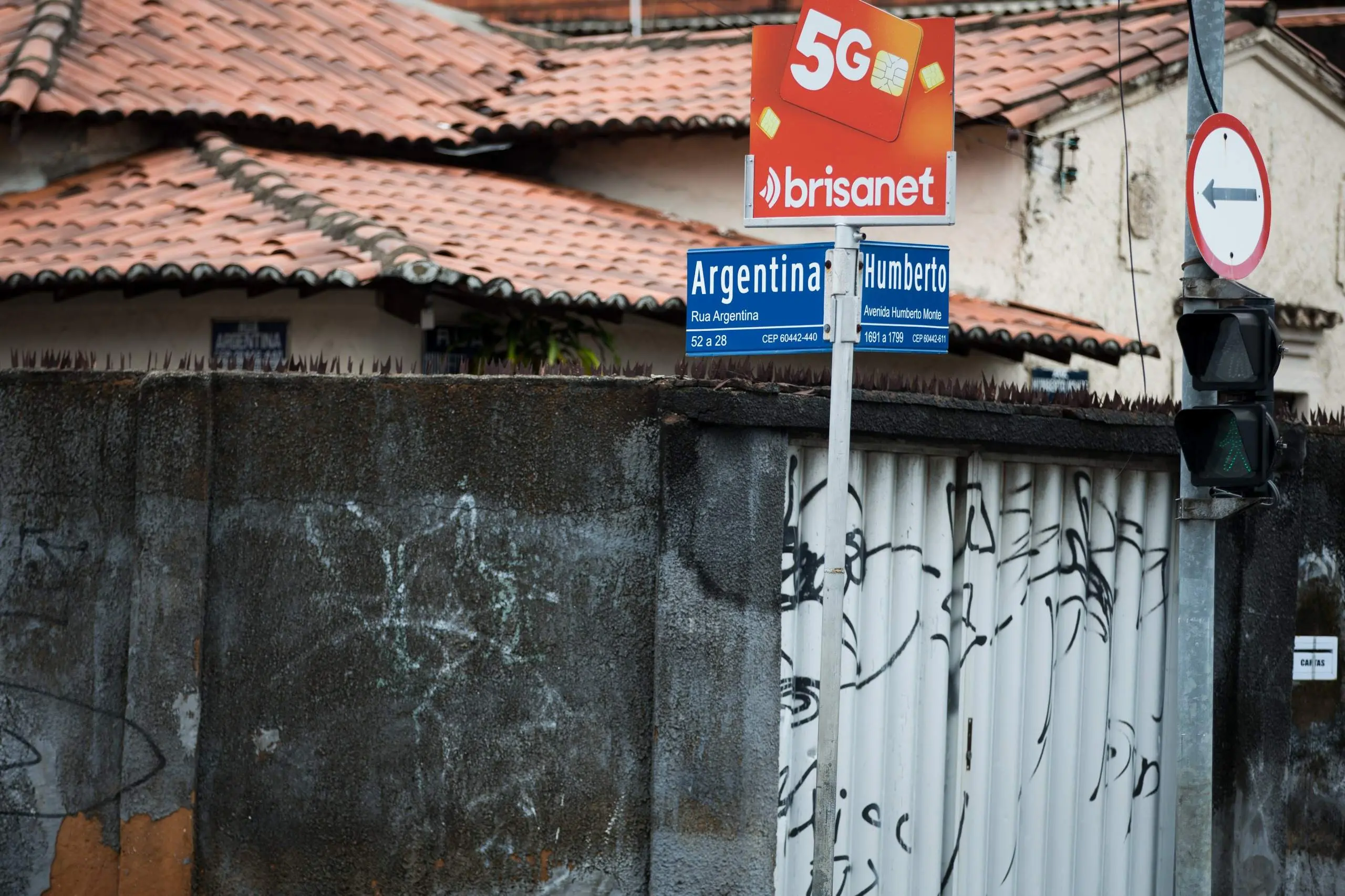 Placas da Rua Argentina e Avenida Humberto Monte. Ao lado, semáforo de pedestres verde e muro com pichações em área urbana de Fortaleza.