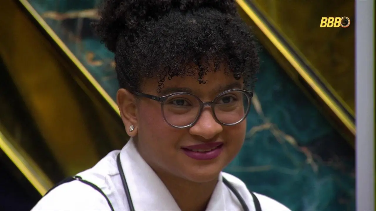 Cena em close-up de Milena na final do BBB 26, em ambiente interno da casa, durante transmissão do programa, com logotipo do BBB no canto da tela.