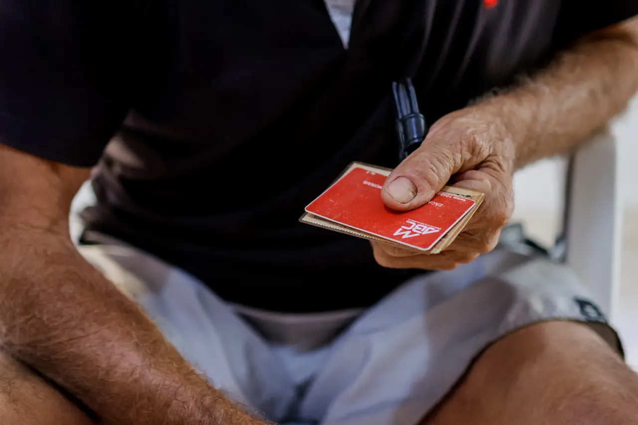 As mãos de um homem seguram um cartão vermelho com a logomarca do Sindicato dos Metalúrgicos do ABC em um plano detalhado.